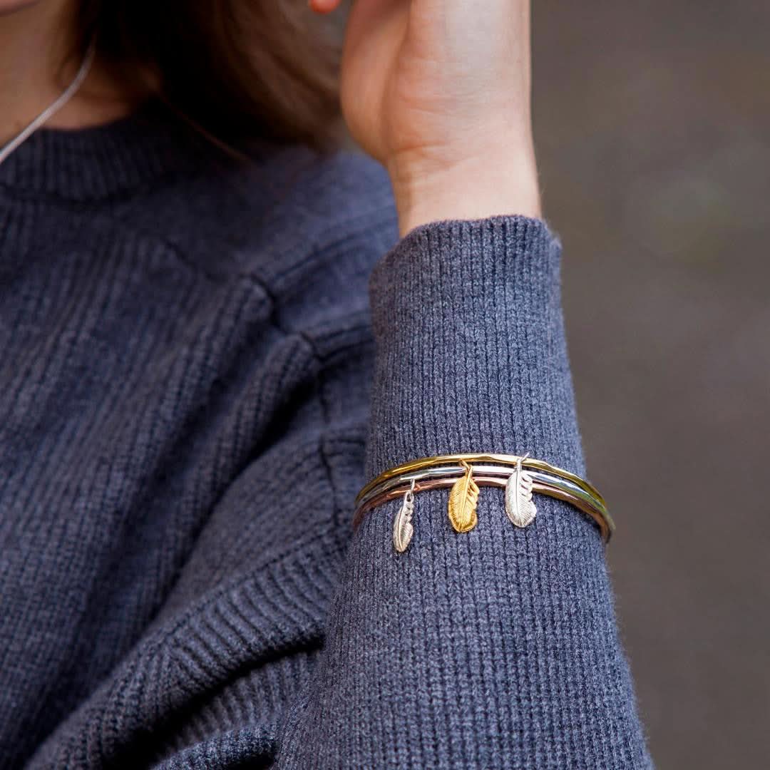 close up of model wearing three feather bangles