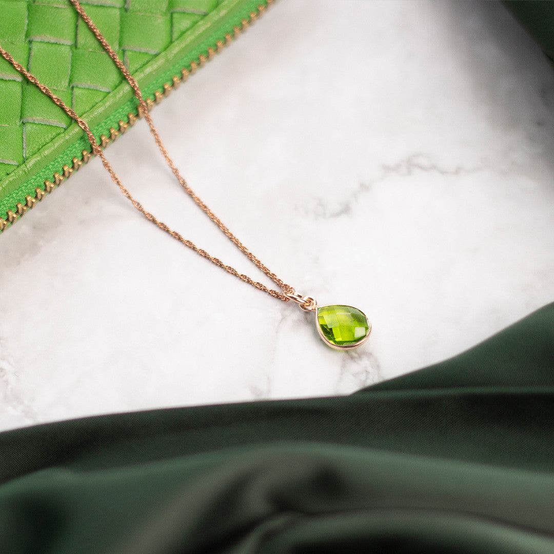 peridot charm necklace in rose gold sitting on marble table with green purse