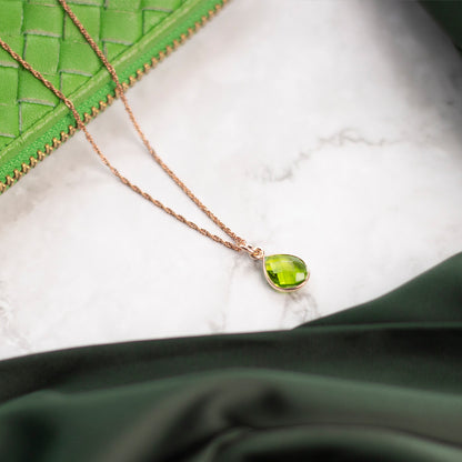 peridot charm necklace in rose gold sitting on marble table with green purse