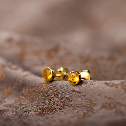 citrine mini stud earrings in gold sitting on a piece of fabric