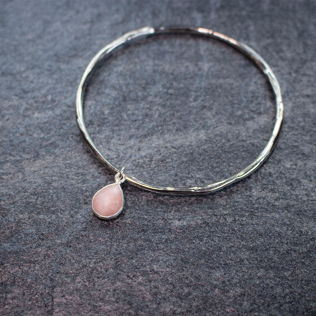 pink opal charm bangle in silver on piece of grey fabric