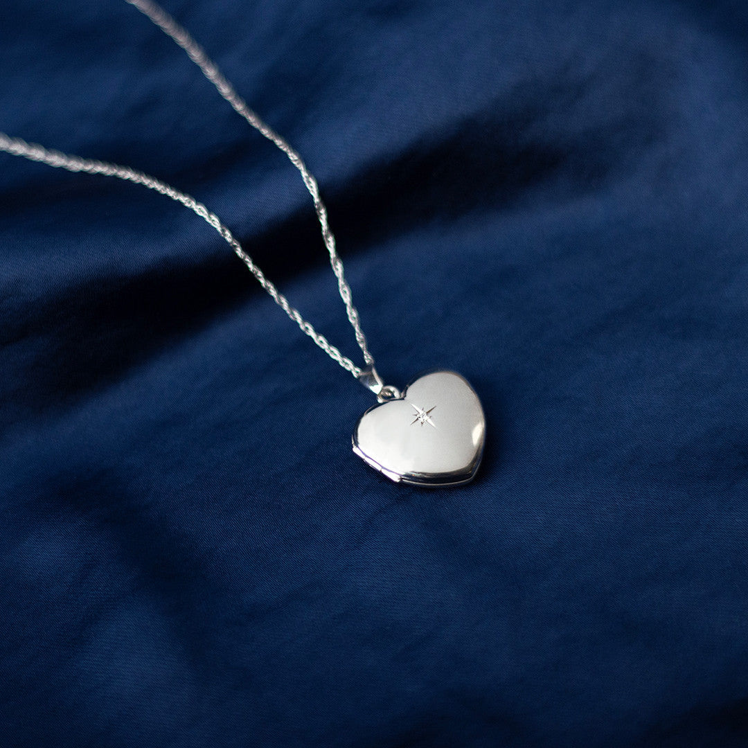 solid white gold diamond heart  locket on a piece of blue fabric