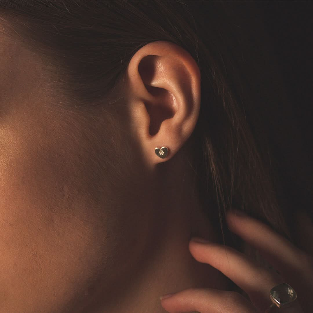 close up of a female model wearing heart shaped stud style earrings in silver with a diamond decoration