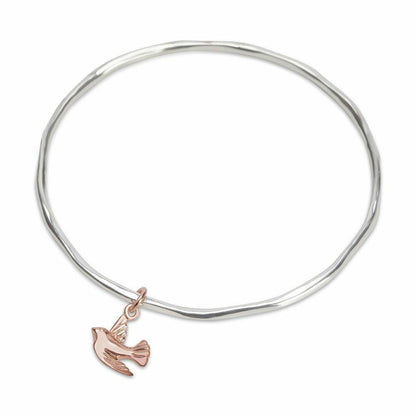 silver bangle with rose gold bird charm on a white background