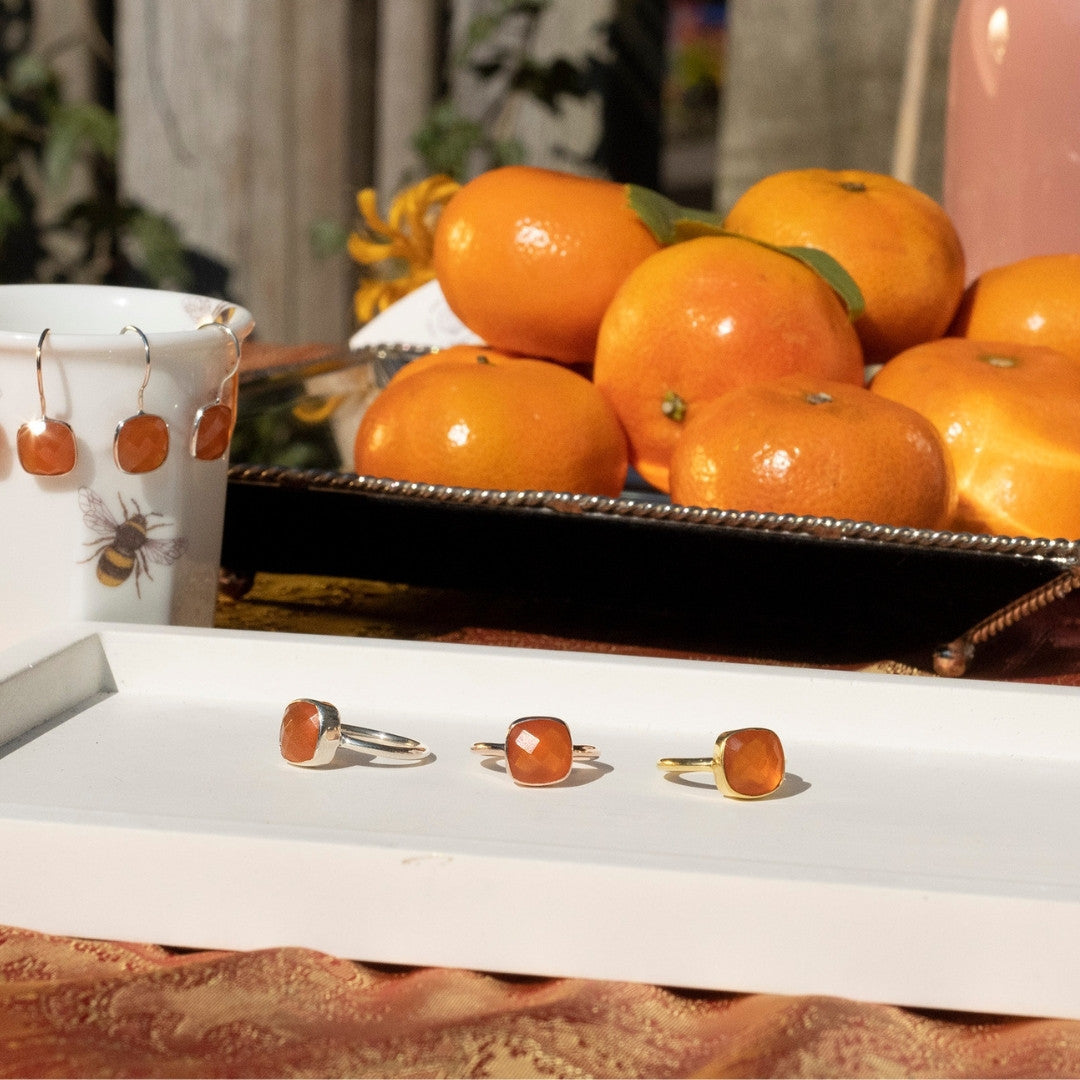 three carnelian cocktail rings next to carnelian luminous earrings and basket of oranges