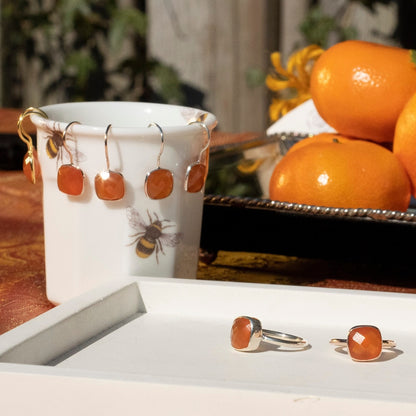 carnelian earrings in gold next to cocktail ring and tray of oranges