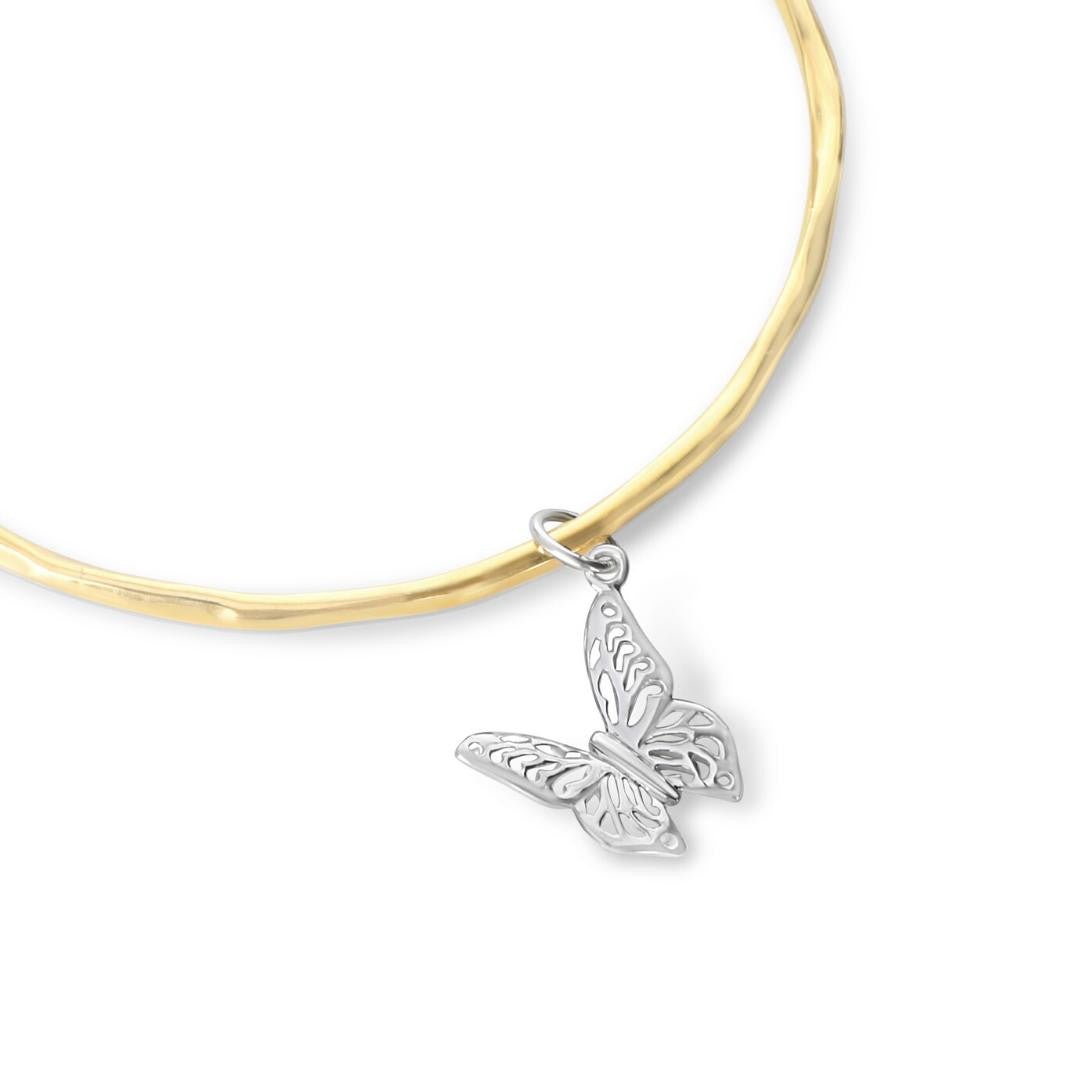 close up of gold bangle with silver butterfly charm on a white background