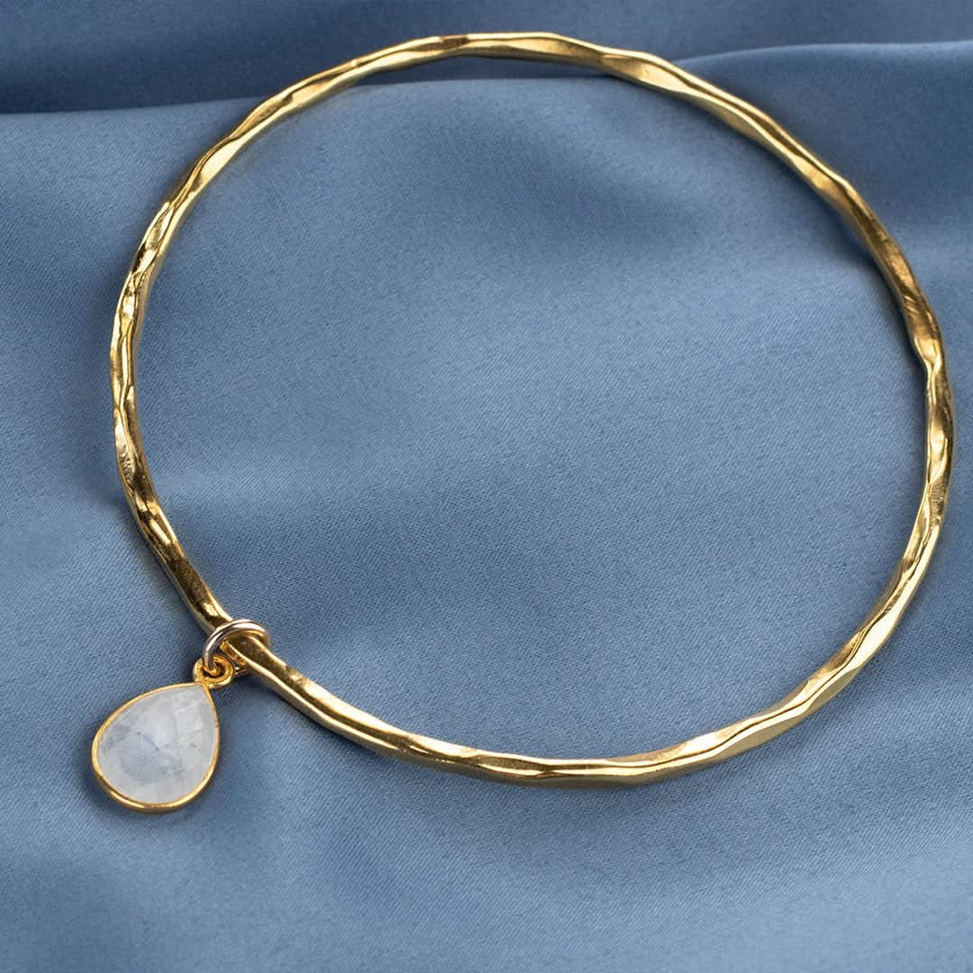 gold moonstone charm bangle on a piece of blue fabric