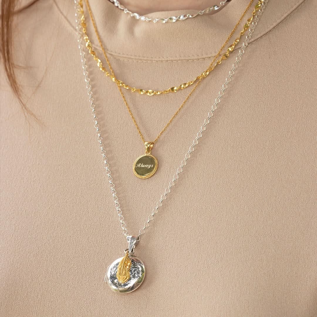 close up of model wearing silver feather locket with gold feather attached