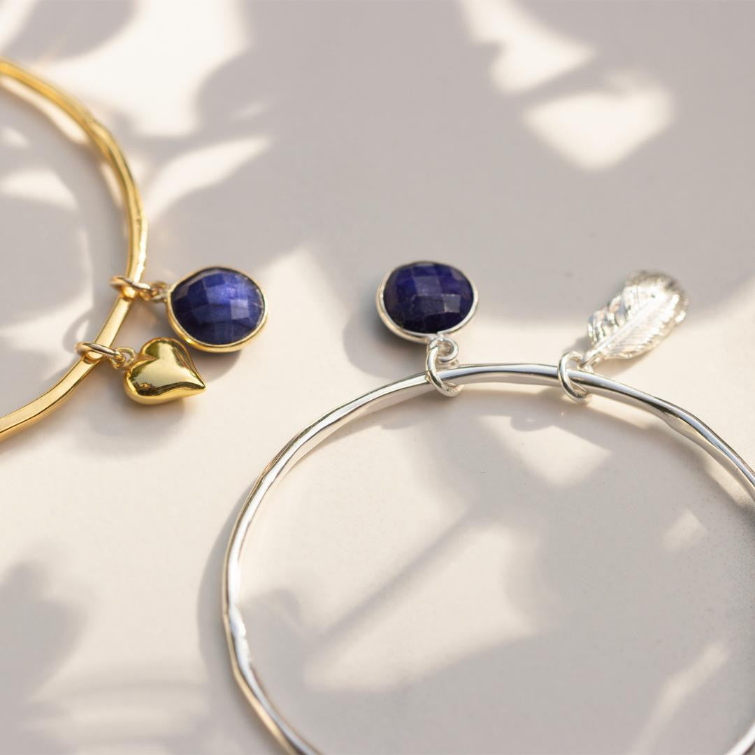 two charm bangles with sapphire charms attached on a white surface