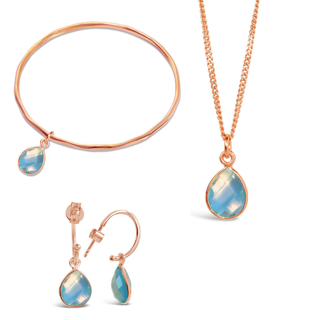 blue topaz rose gold charm bangle, necklace and drop hoop earrings on a white background