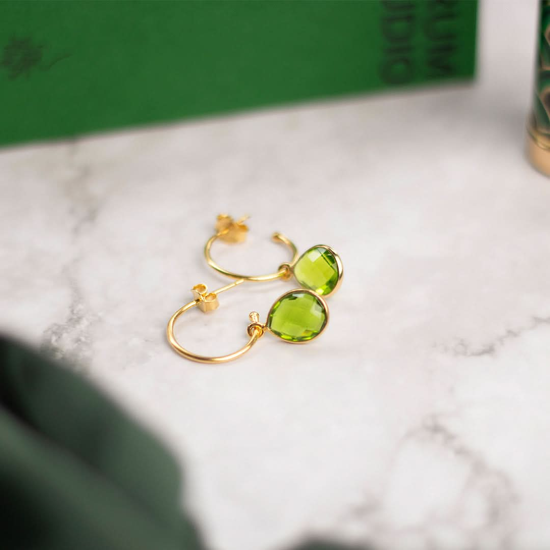 peridot drop hoop earrings in gold on a marble table