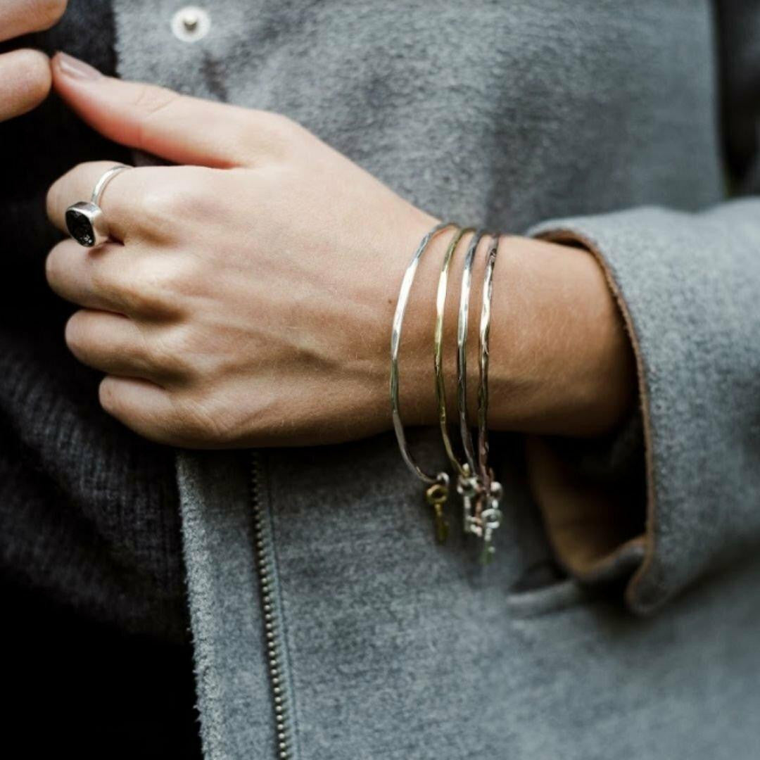 close up of model wearing four silver bangles with key charms attached 