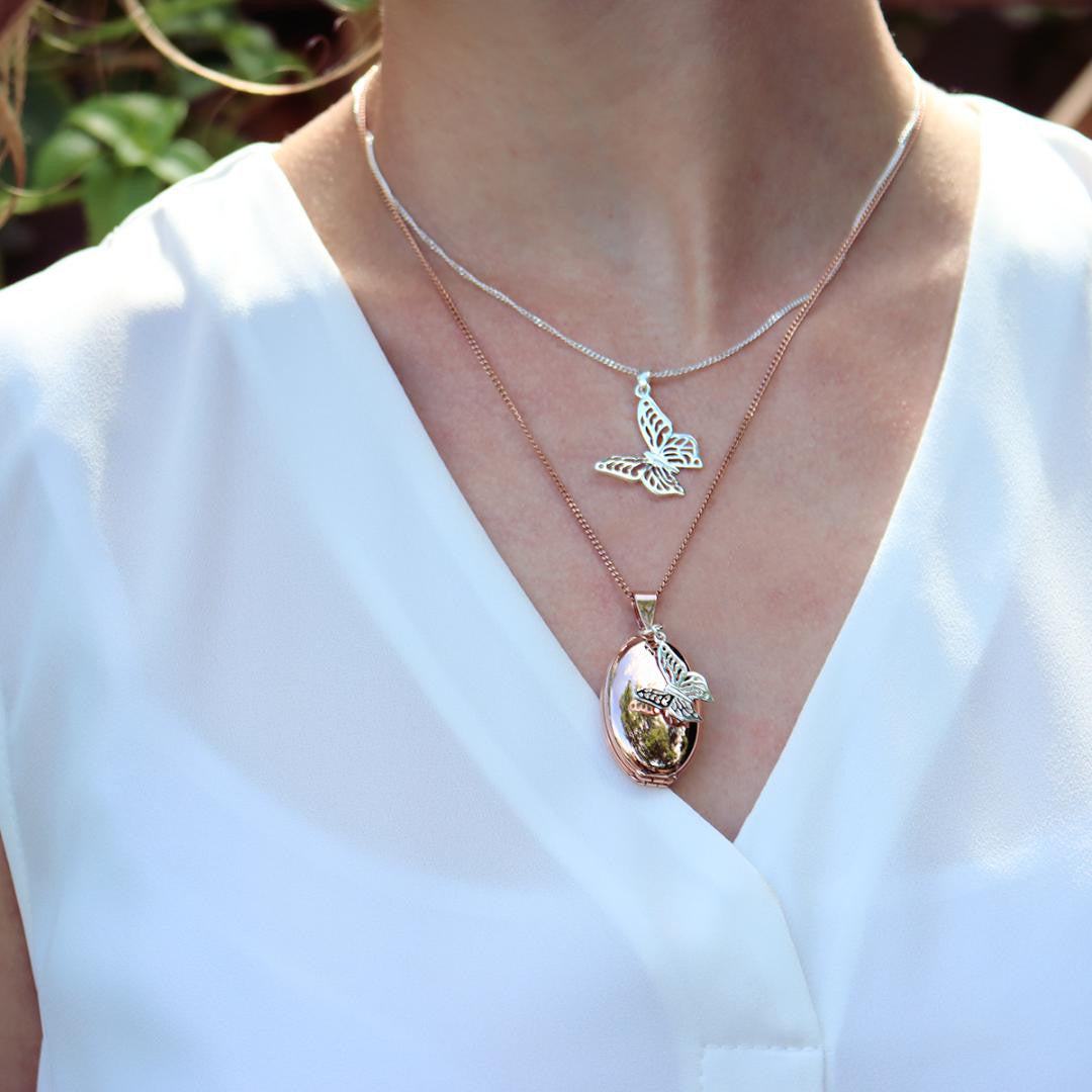 model in white top wearing silver oval shaped locket with butterfly charm