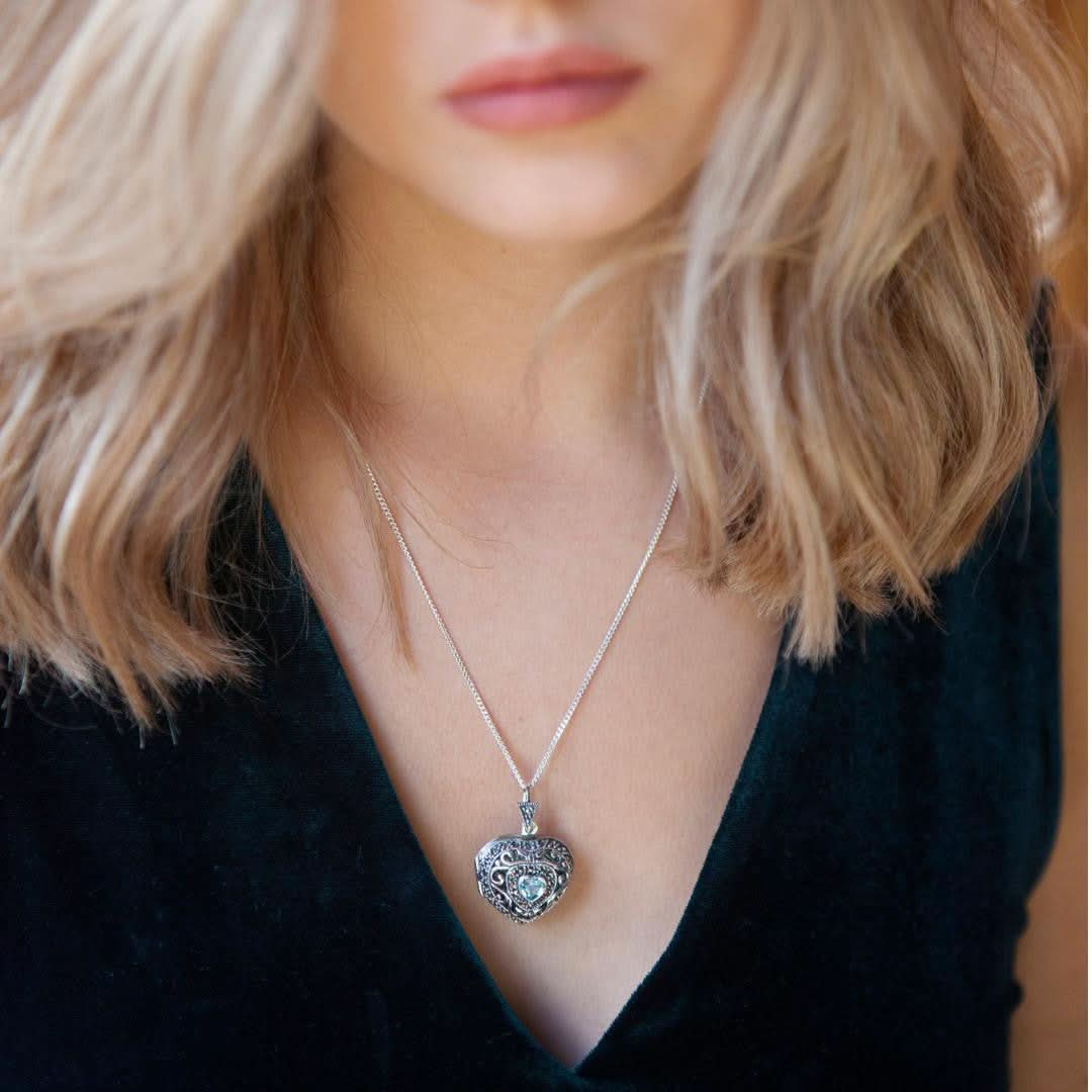 Model in black top wearing silver vintage heart locket with topaz gemstone