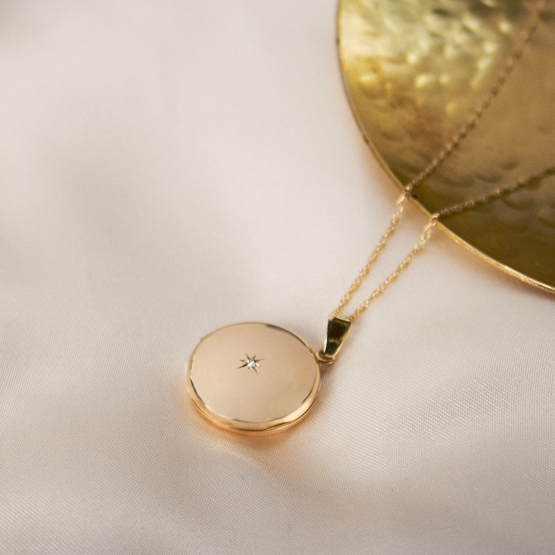 round diamond locket in gold next to gold plate