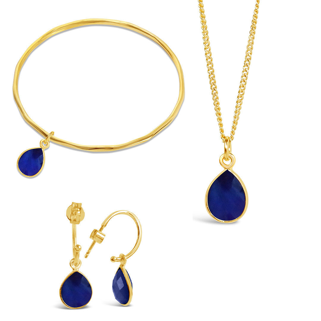 gold sapphire charm bangle, necklace and drop hoop earrings on a white background