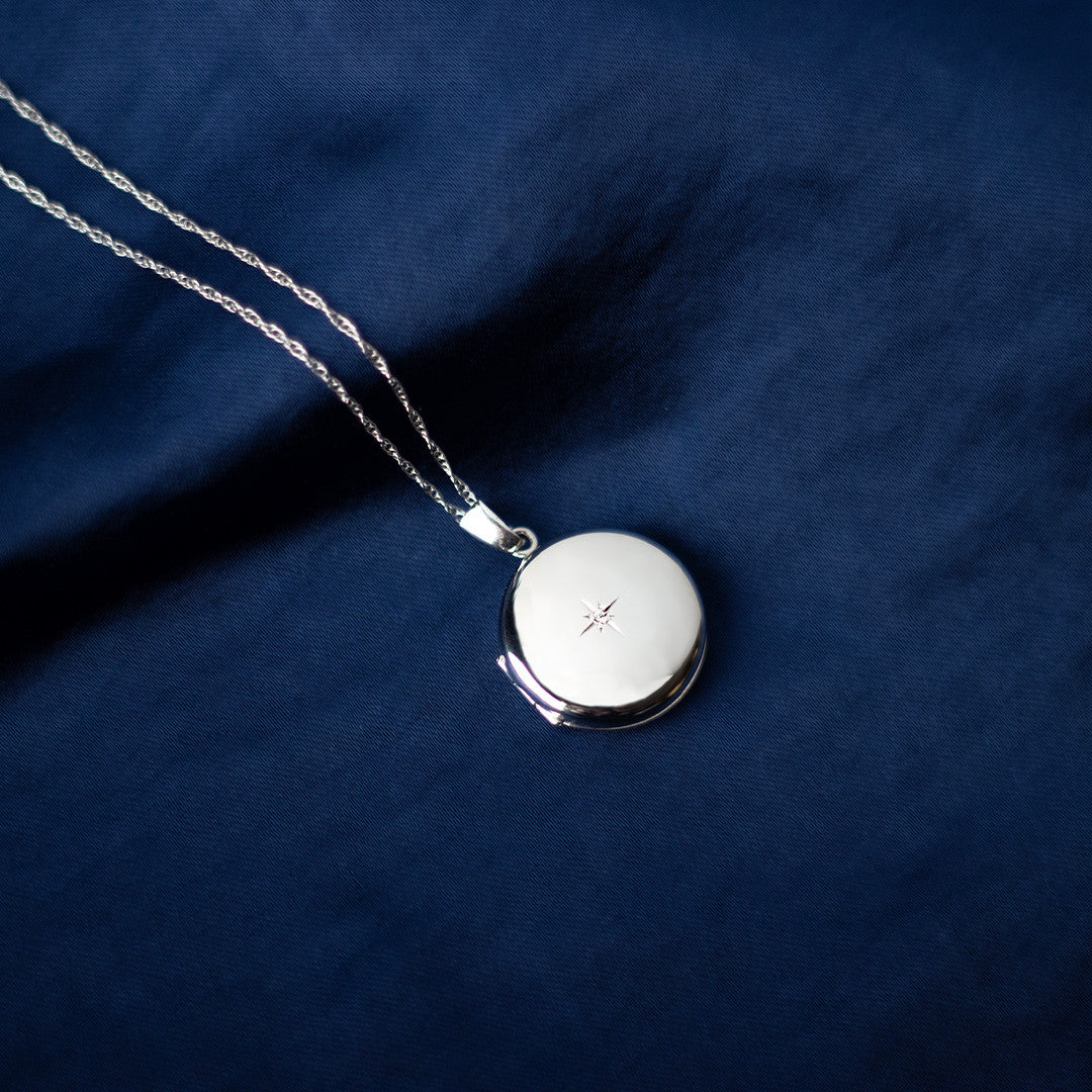 white gold diamond round locket on a piece of blue fabric