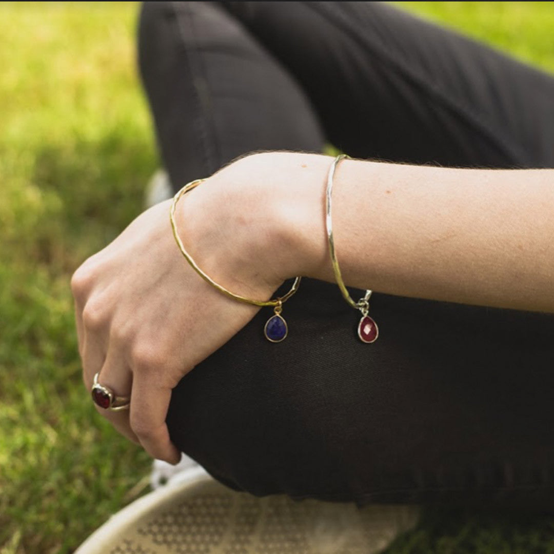 close up of model wearing two gold charm bangles with birthstones