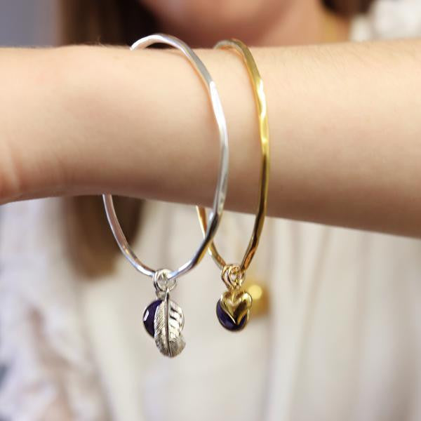 close up of model wearing two sapphire charm bangles with different charms 