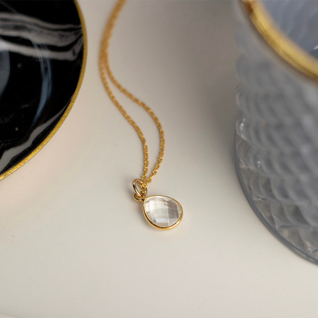 white quartz charm necklace in gold next to a glass