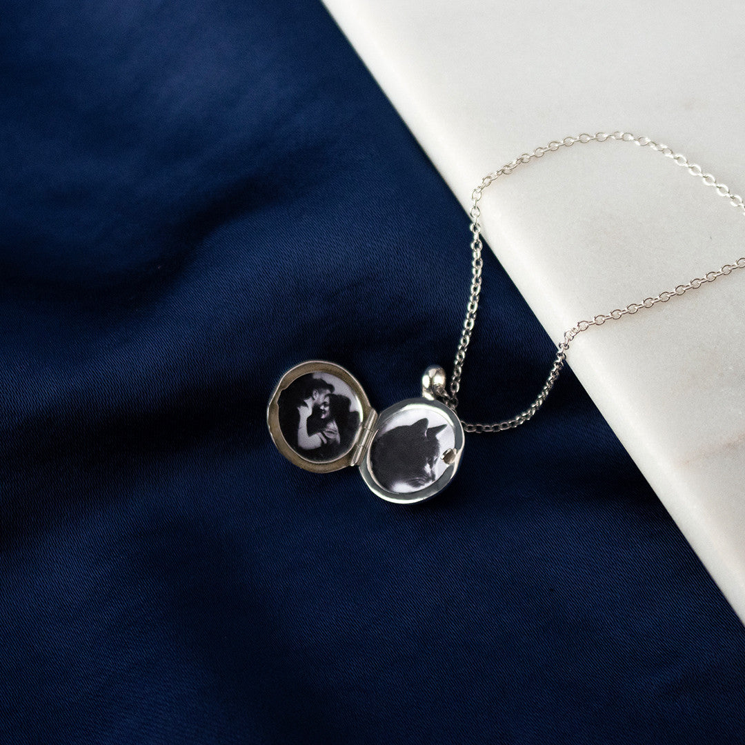 opened small round diamond locket in silver on a piece of blue fabric