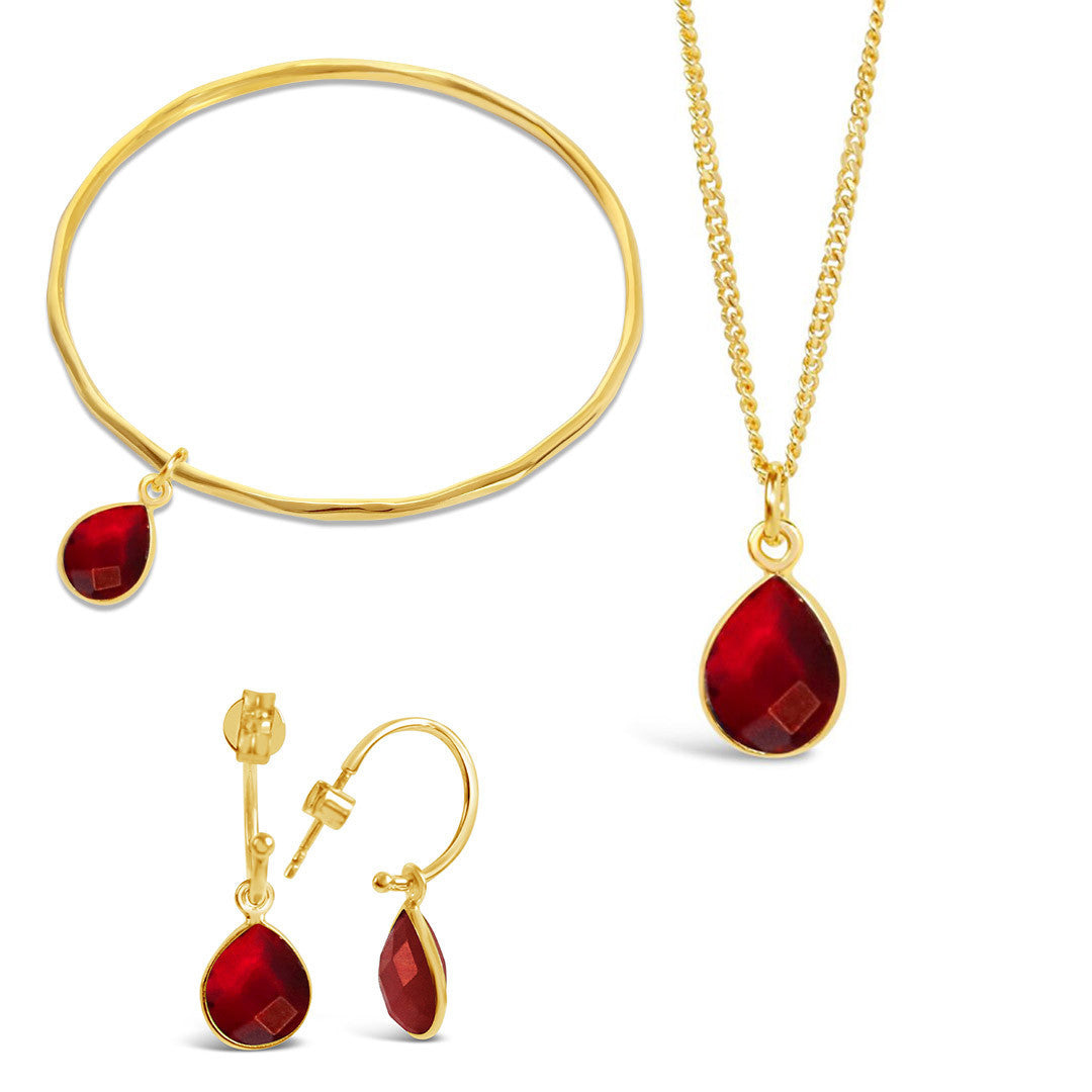 gold garnet charm bangle, necklace and drop hoop earrings on a white background