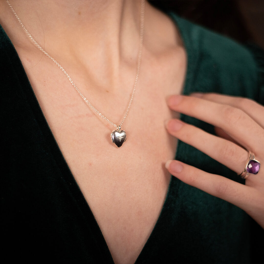 closeup of model wearing a heart shaped locket in silver on a silver chain with a diamond decoration