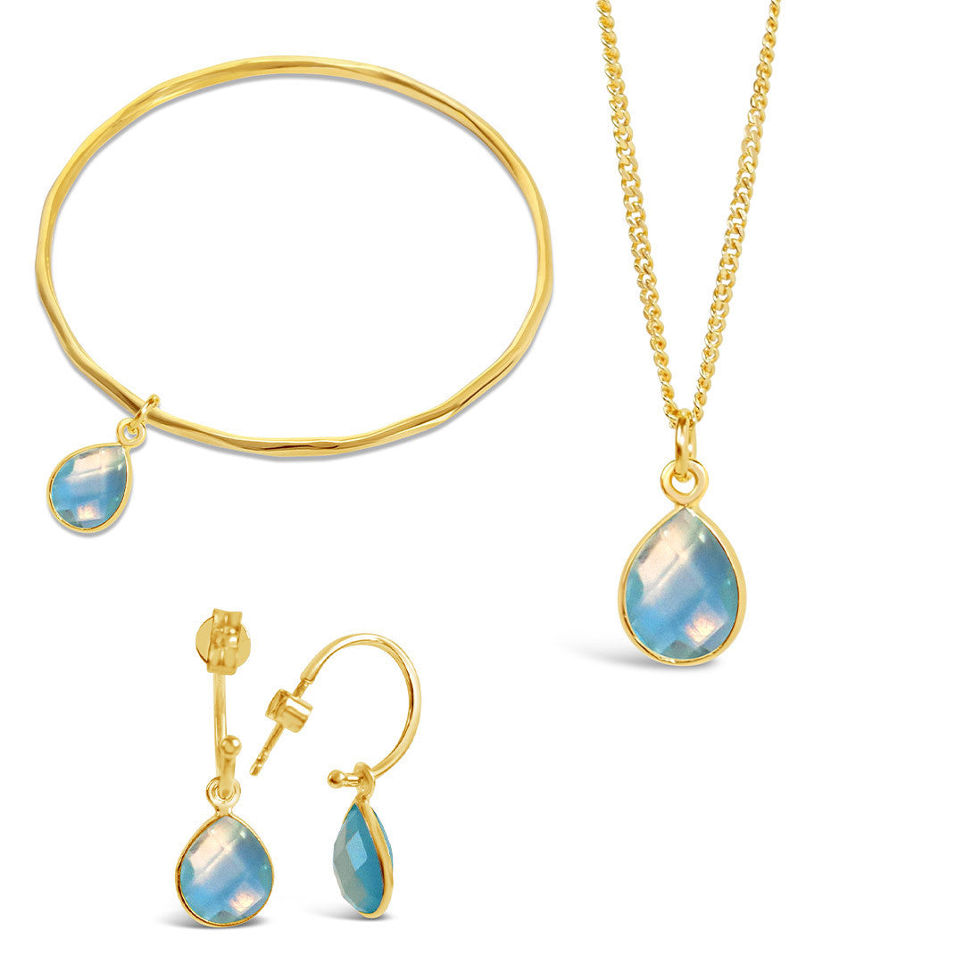 gold blue topaz charm bangle, necklace and drop hoop earrings on a white background
