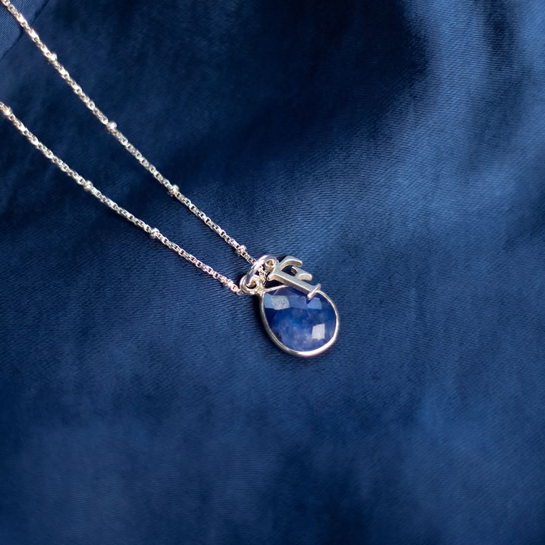 sapphire charm necklace in silver with initial charm on a blue piece of fabric