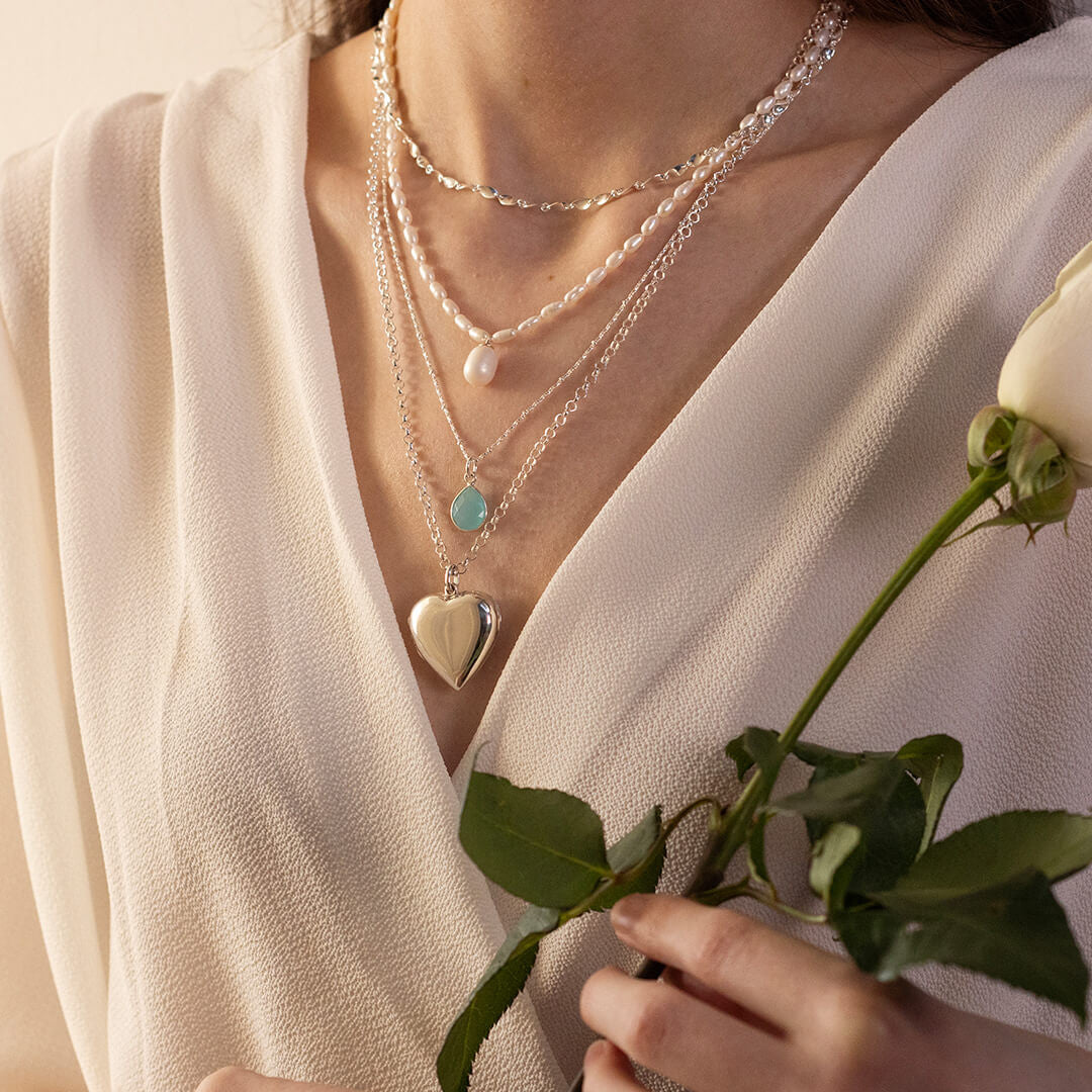 close up of model wearing large two photo heart locket in silver whilst holding flowers