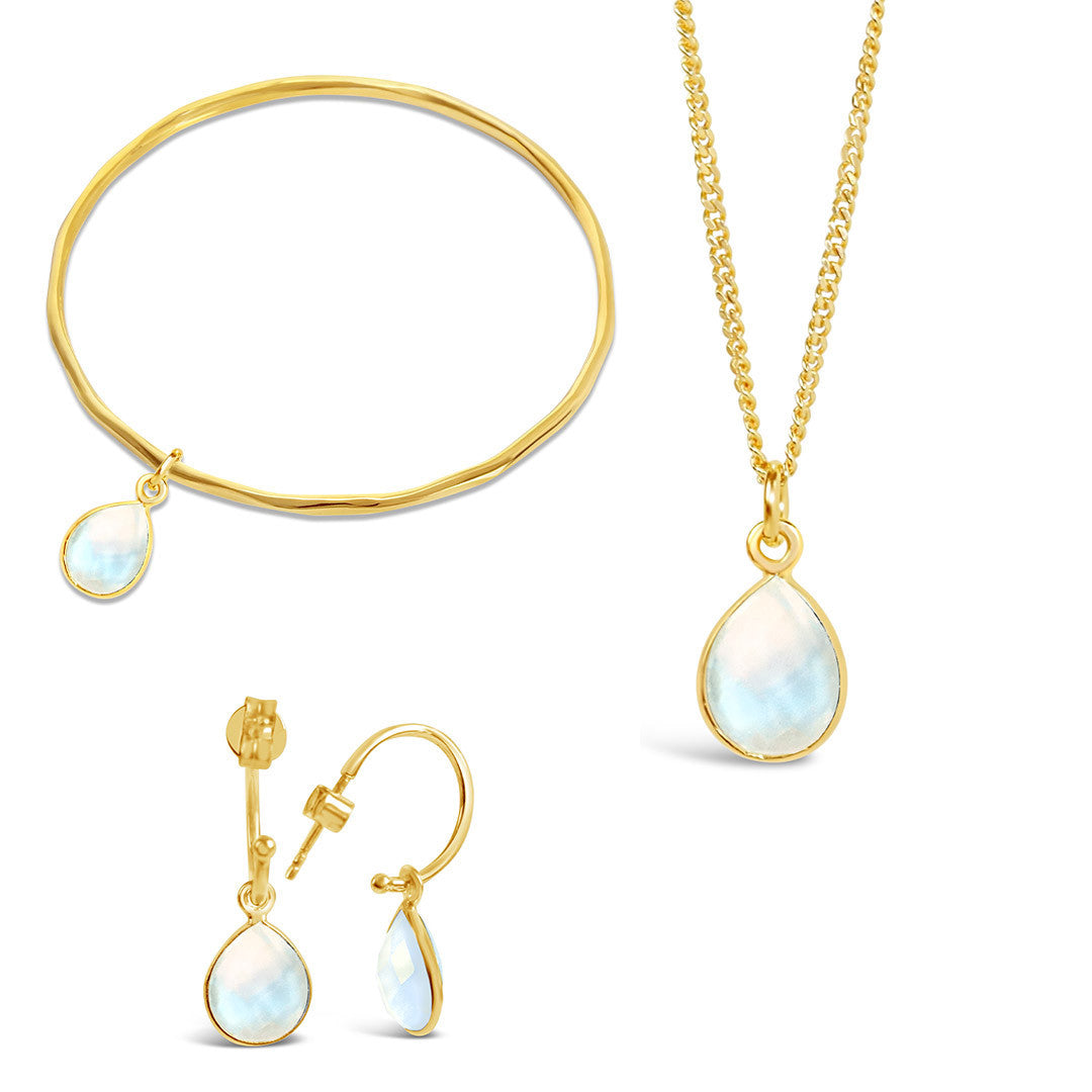 gold moonstone charm bangle, necklace and drop hoop earrings on a white background