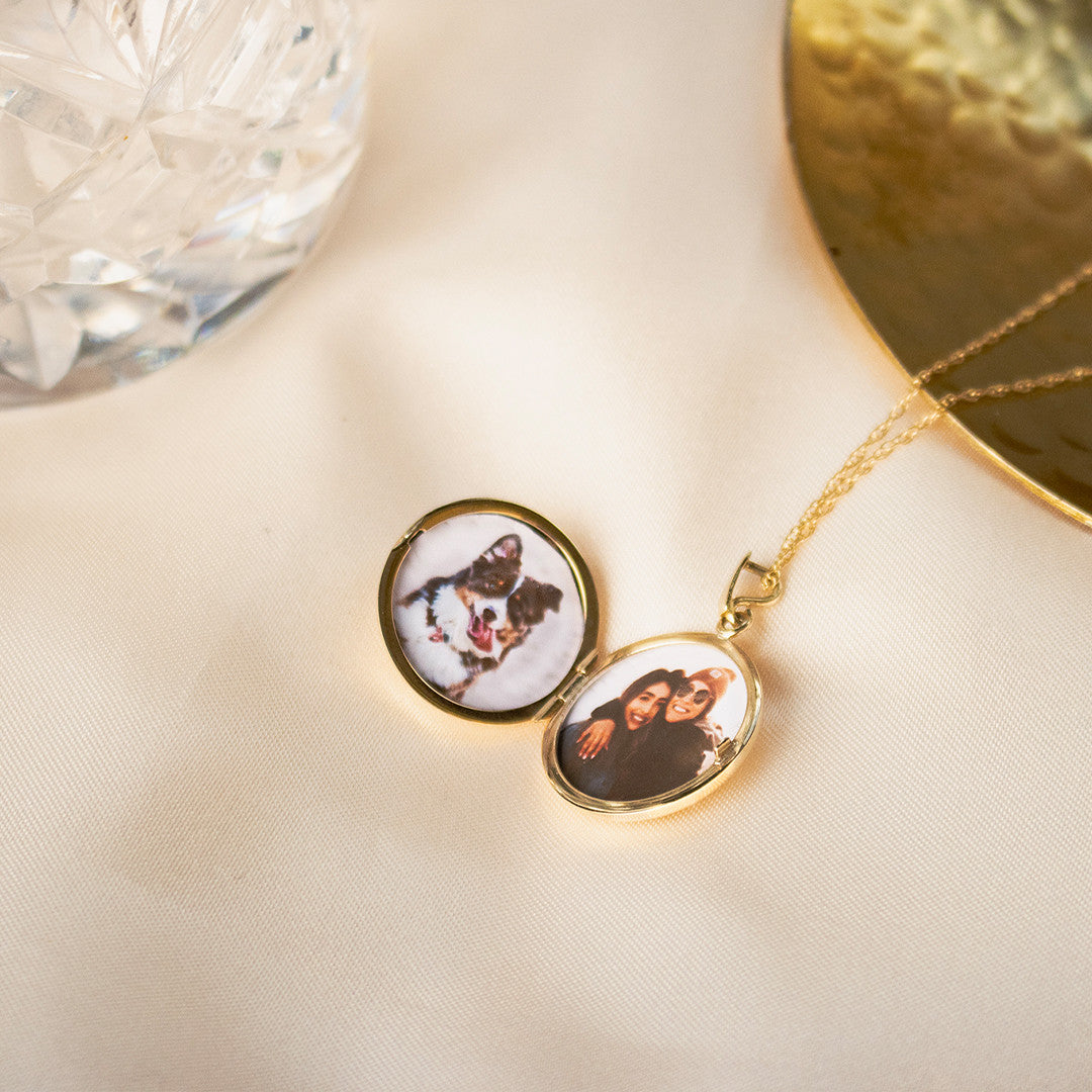 opened gold round diamond locket with family photos inside next to glass
