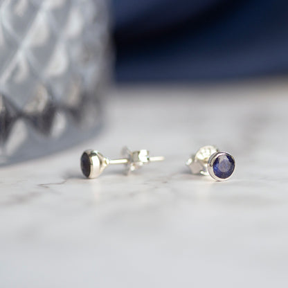 Sapphire mini stud earrings in silver laid out on a marble surface