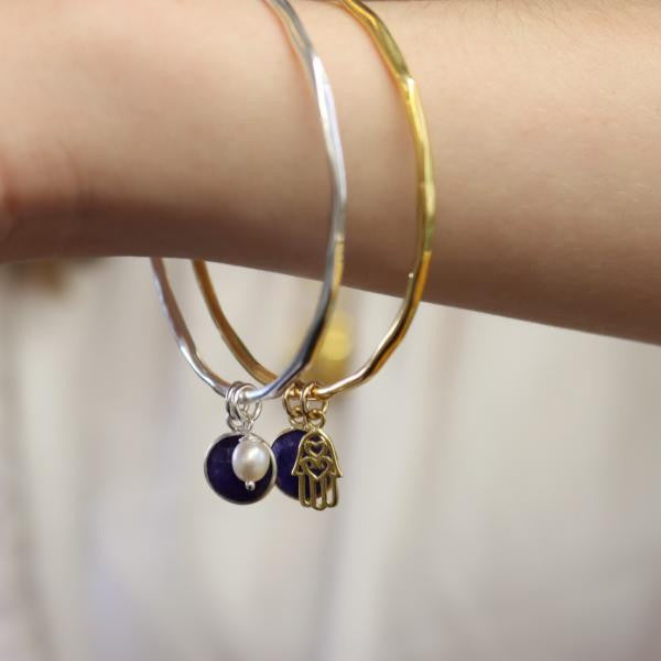 model wearing two sapphire charm bangles with different charms