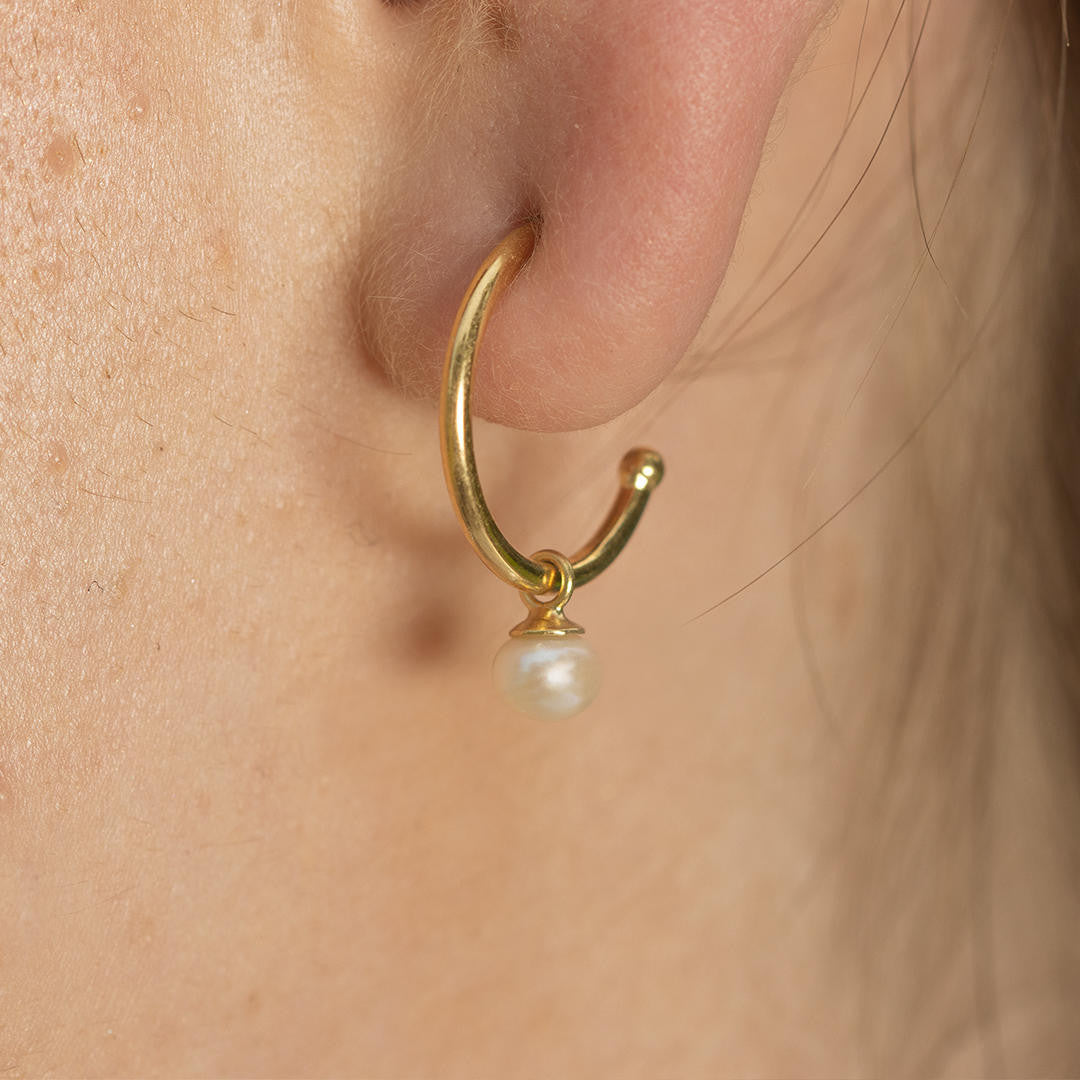 close up of model wearing dainty pearl drop hoop earrings in ivory gold