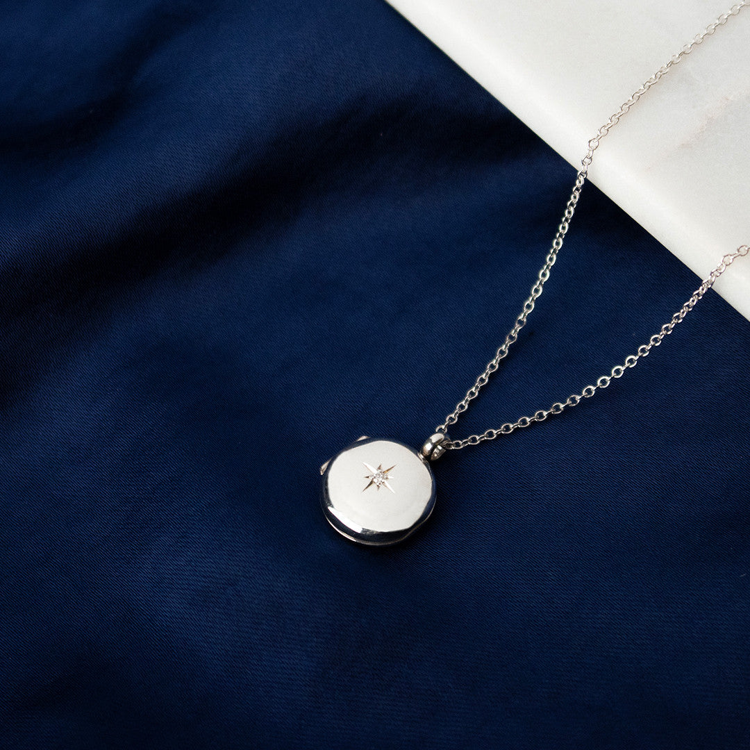 small round diamond locket in silver on a piece of blue fabric