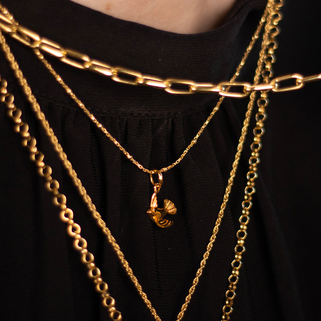 model wearing bird pendant in gold along with other gold chains