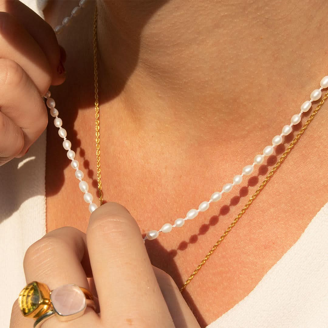 Model touching an ivory seed pearl necklace which she is wearing