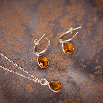 citrine charm necklace and drop hoop earrings in silver on a piece of fabric